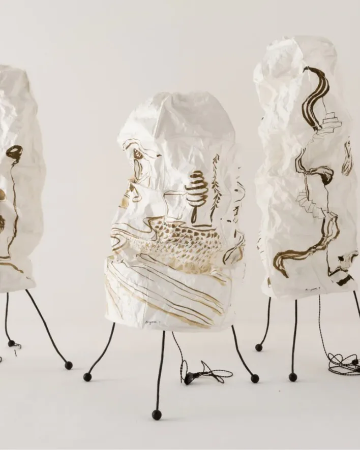 Four translucent sculptural heads with organic line drawings in ink, mounted on thin black stems against white background.