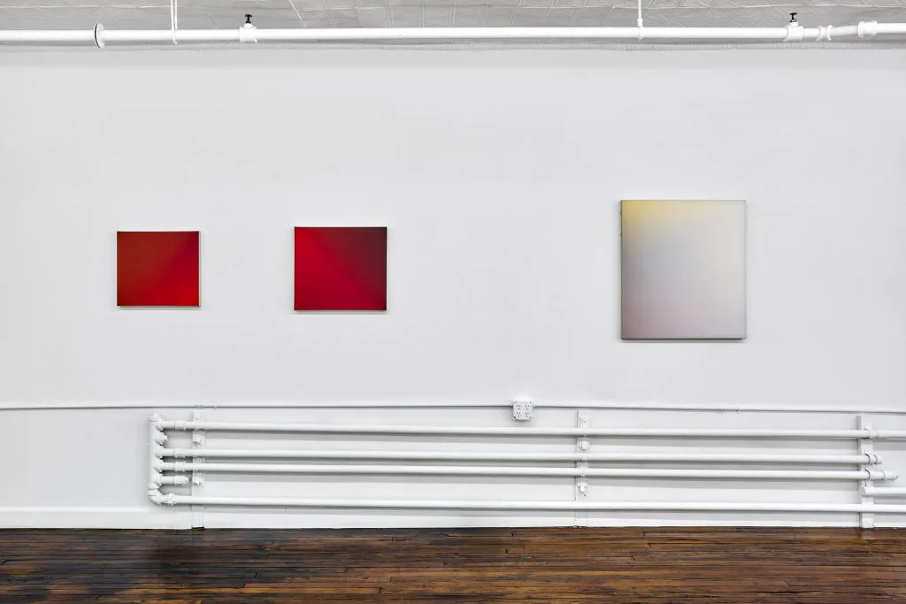 Off Paradise gallery wall displaying three artworks: two red squares and one gradient square, with fluorescent lighting below.