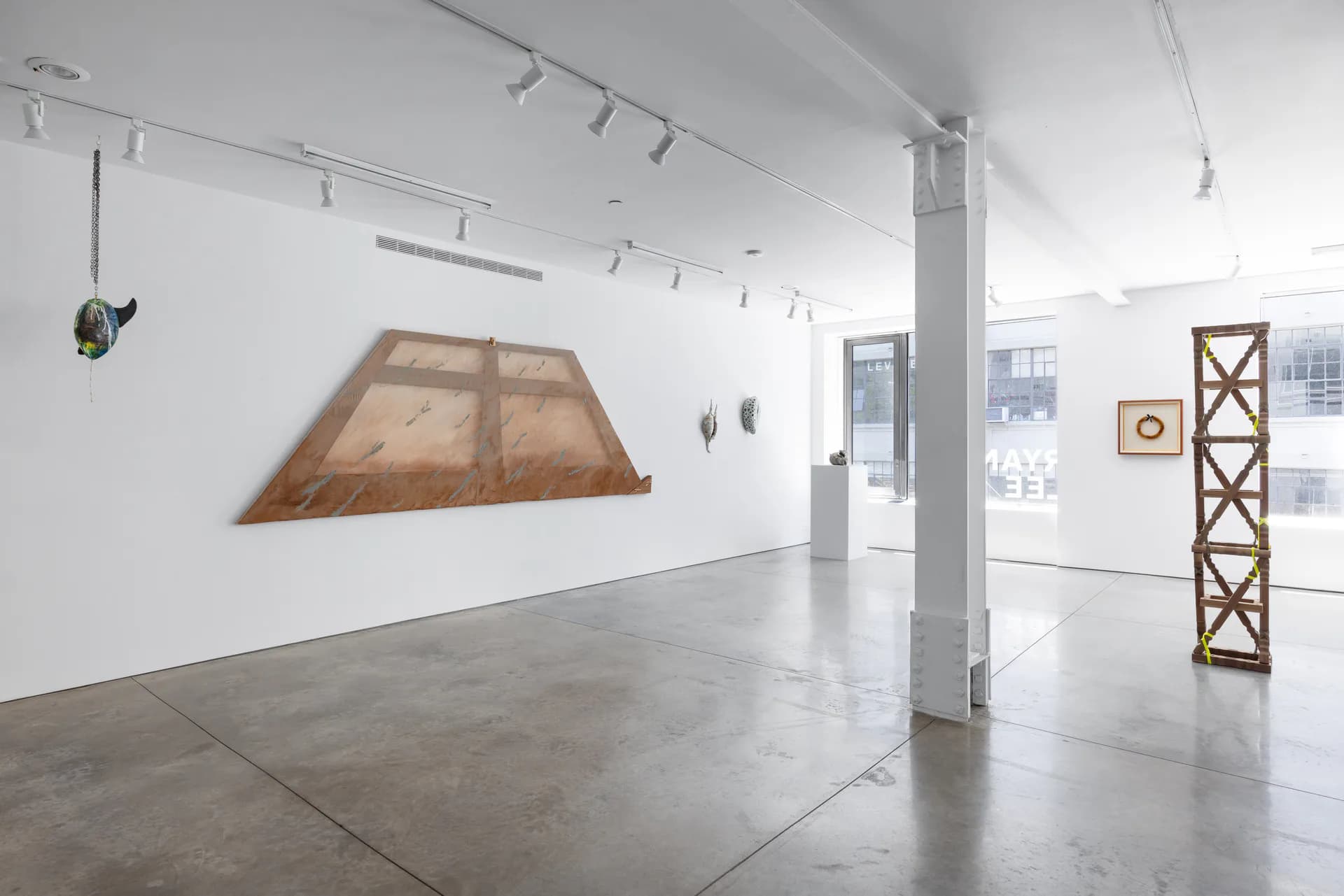 Minimalist white gallery interior with polished concrete floor, wooden and geometric sculptural installations mounted on walls and ceiling.