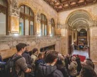 Historic ornate corridor with arched ceilings, stone columns, and tall windows; a crowd of visitors walks through the classical architectural space.