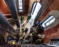Overhead view of a brick building's rooftop with large sculptural blue and white pipes or ducts creating an abstract geometric composition.