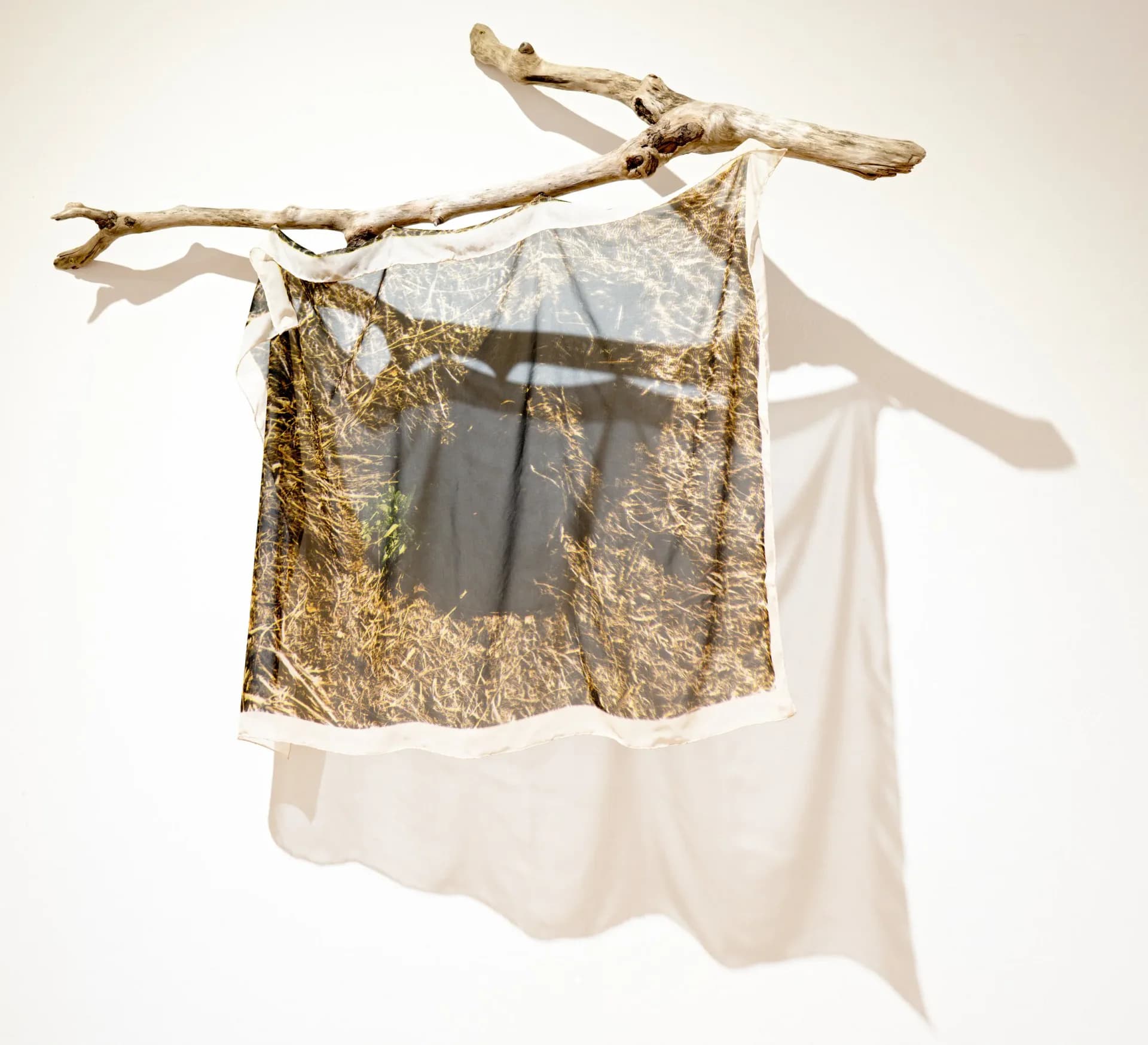 Textile and natural materials sculpture: golden fabric and white cloth suspended from a weathered driftwood branch.