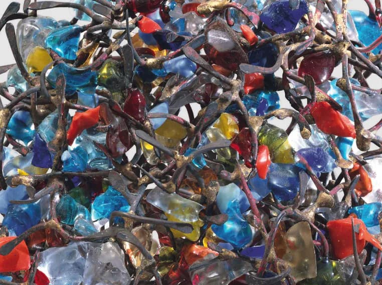 Mixed-media collage of colorful translucent glass or resin fragments in blues, reds, yellows, and greens interwoven with metallic wire or string.