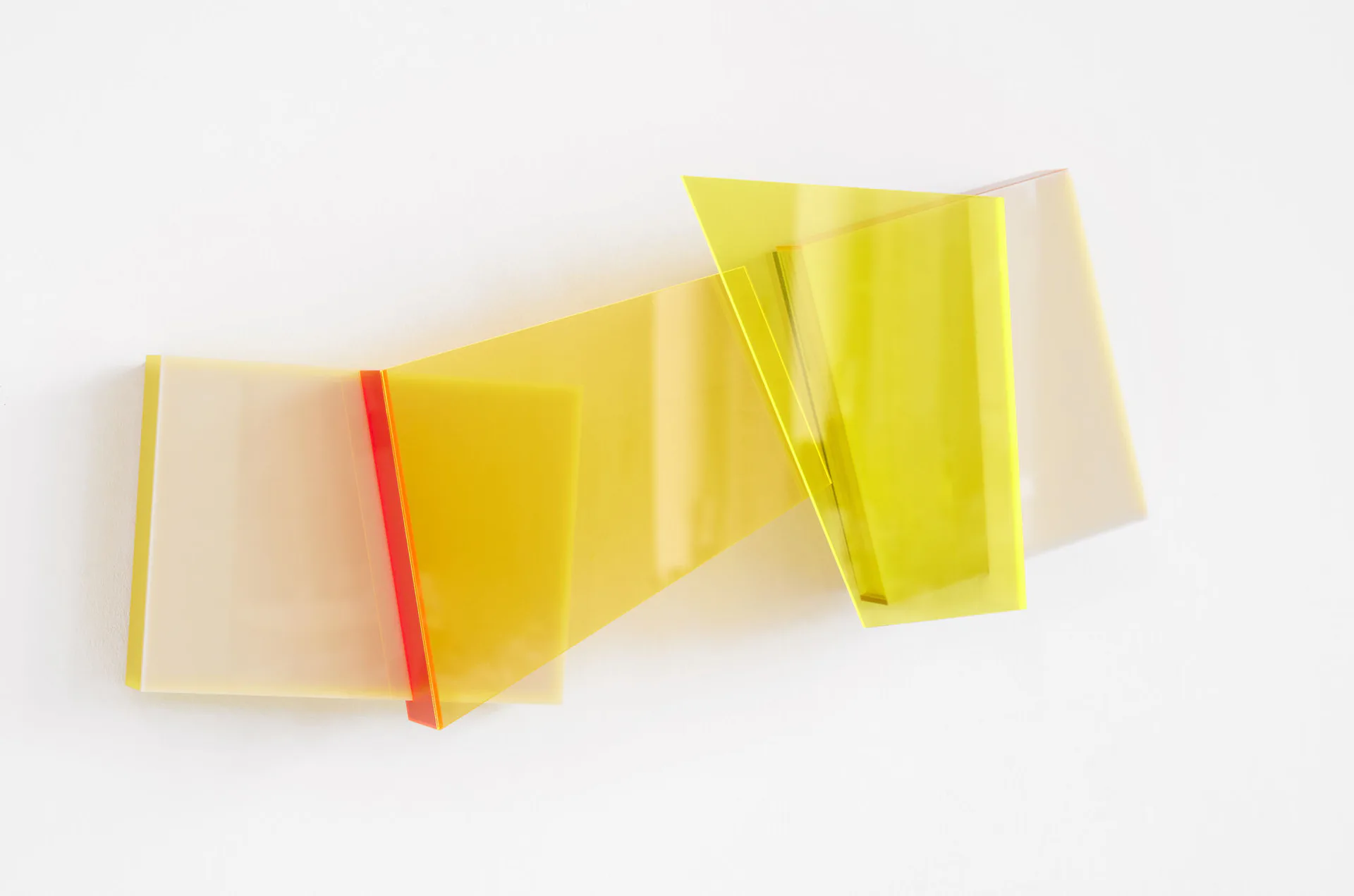 Abstract sculptural installation of translucent yellow and clear acrylic or resin forms folded and stacked in undulating composition.