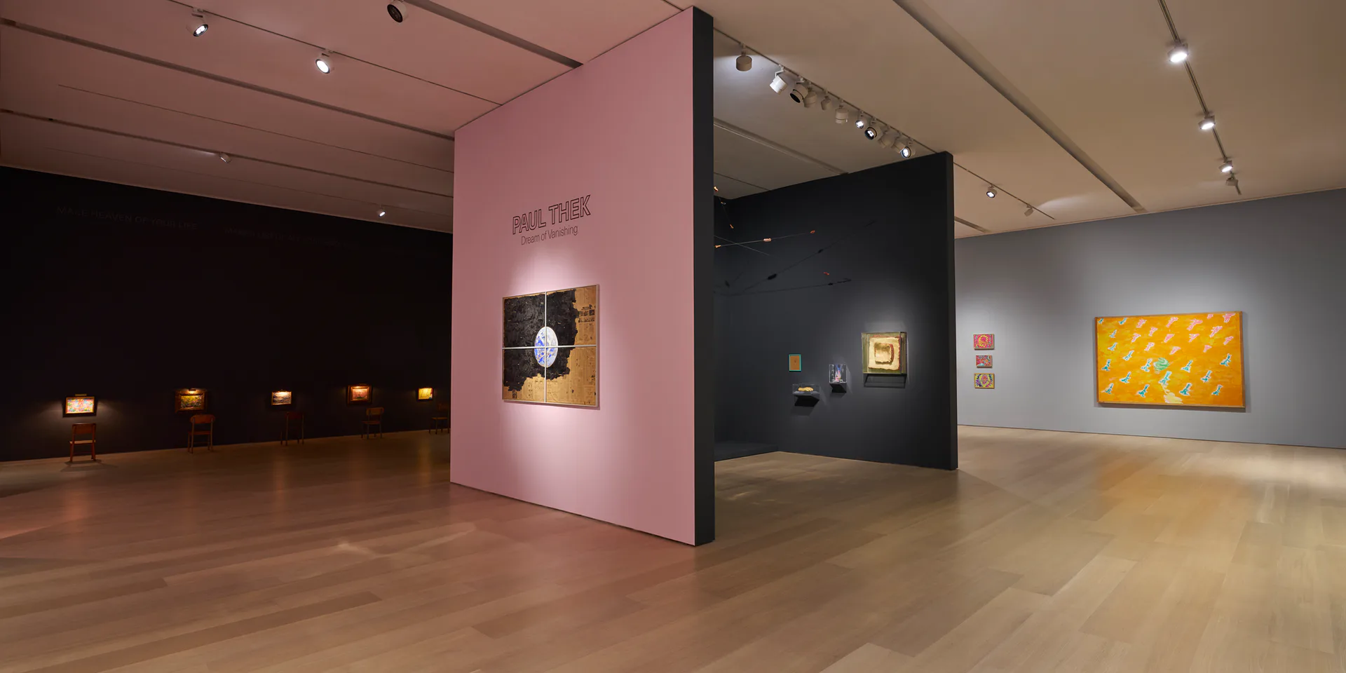 Contemporary gallery interior with pink and black partition walls, wooden floor, small framed artworks, and a large yellow abstract painting visible in background.