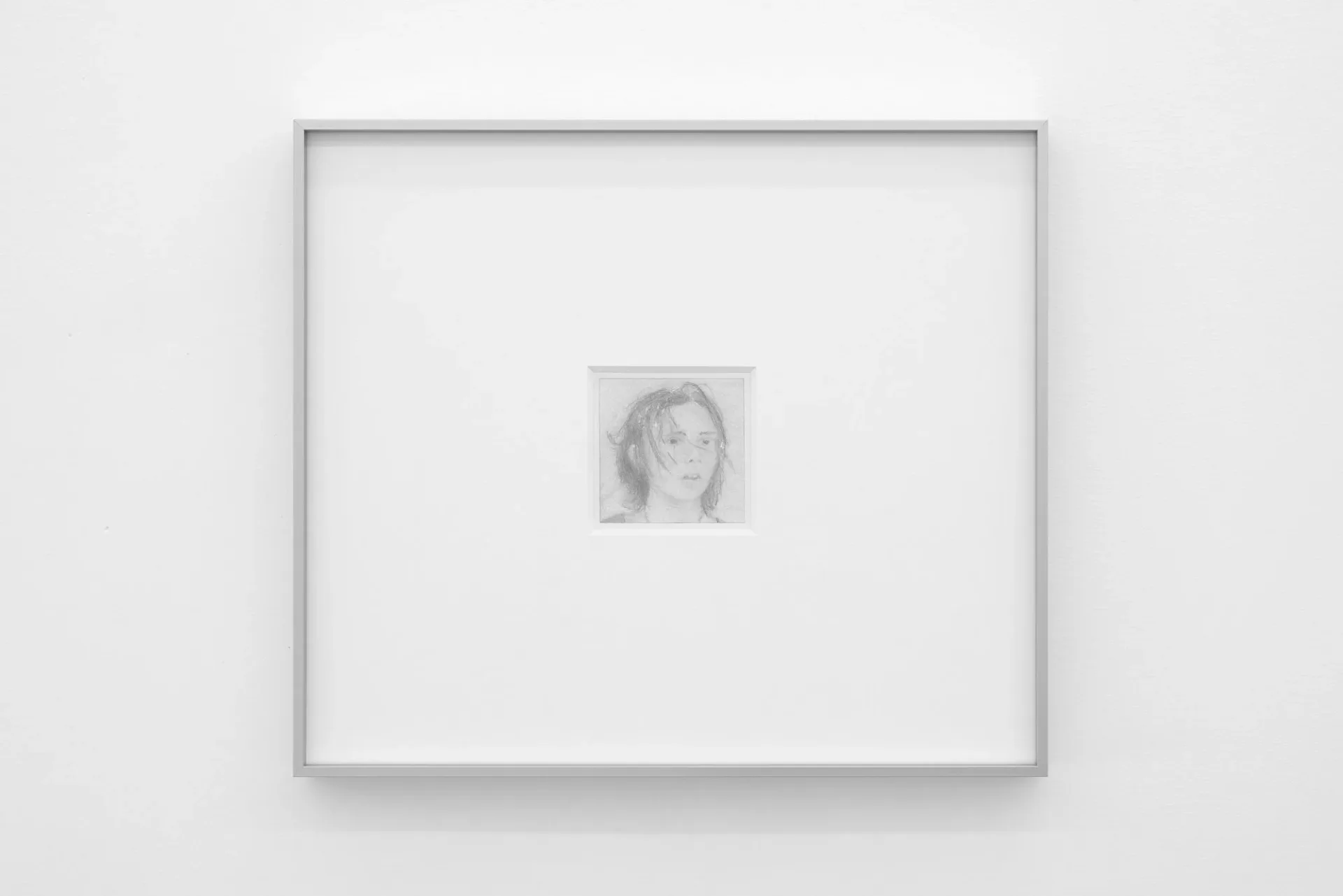 Gallery wall with gray frame displaying a small portrait drawing of a woman's face centered on white matting.