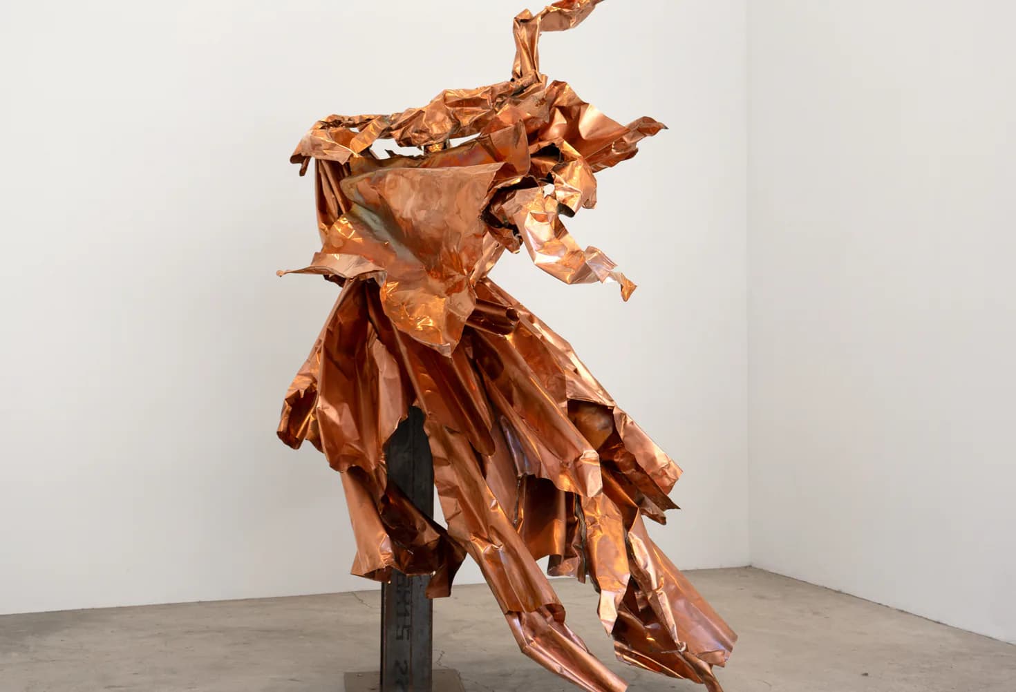 Abstract copper or bronze sculptural form with jagged, organic shapes mounted on a dark base in a white gallery space.