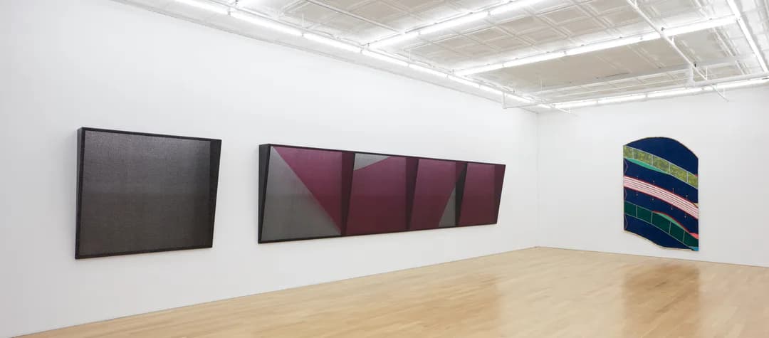Peter Blum Gallery interior with white walls, wooden floor, and three abstract paintings displayed: a dark rectangular work, a burgundy multi-panel composition, and a striped geometric piece.