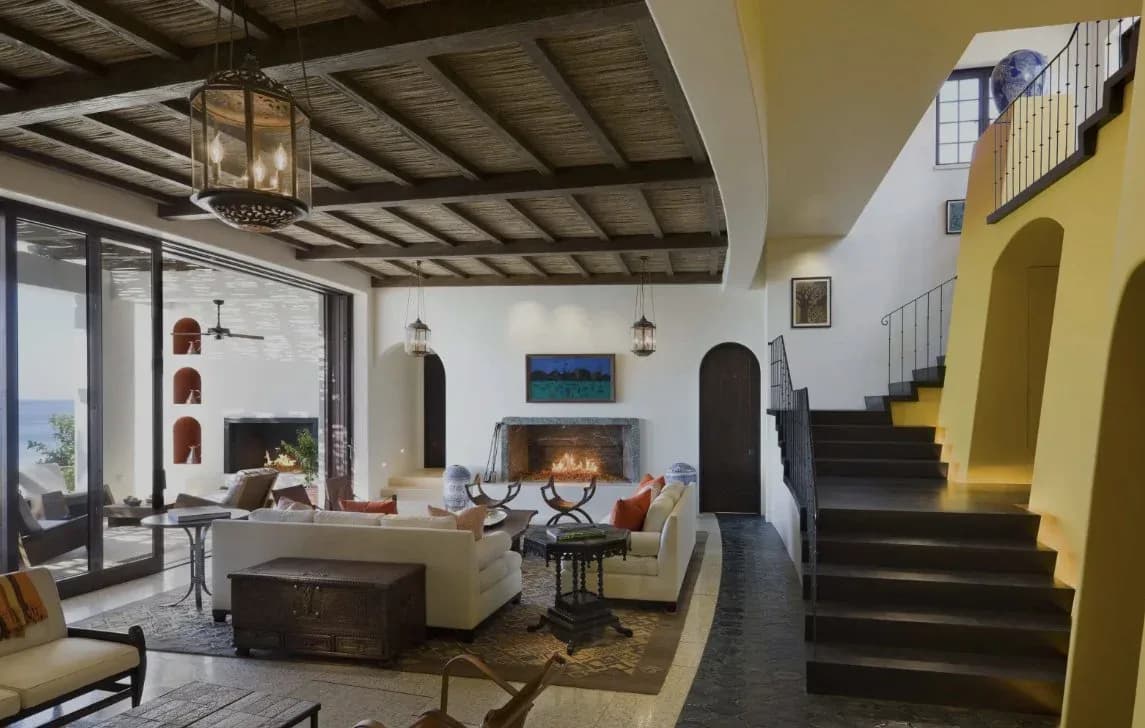 Contemporary loft space with exposed ceiling beams, yellow accent wall, fireplace, cream seating, and industrial staircase.