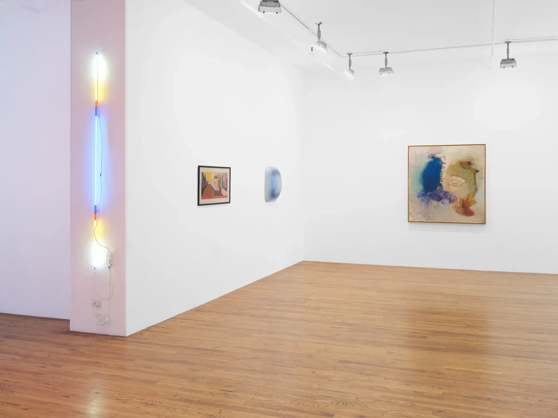 Same gallery view with wooden floor, white walls, track lighting, neon installation on pillar, and three framed pieces displaying blue abstracts and watercolor works.
