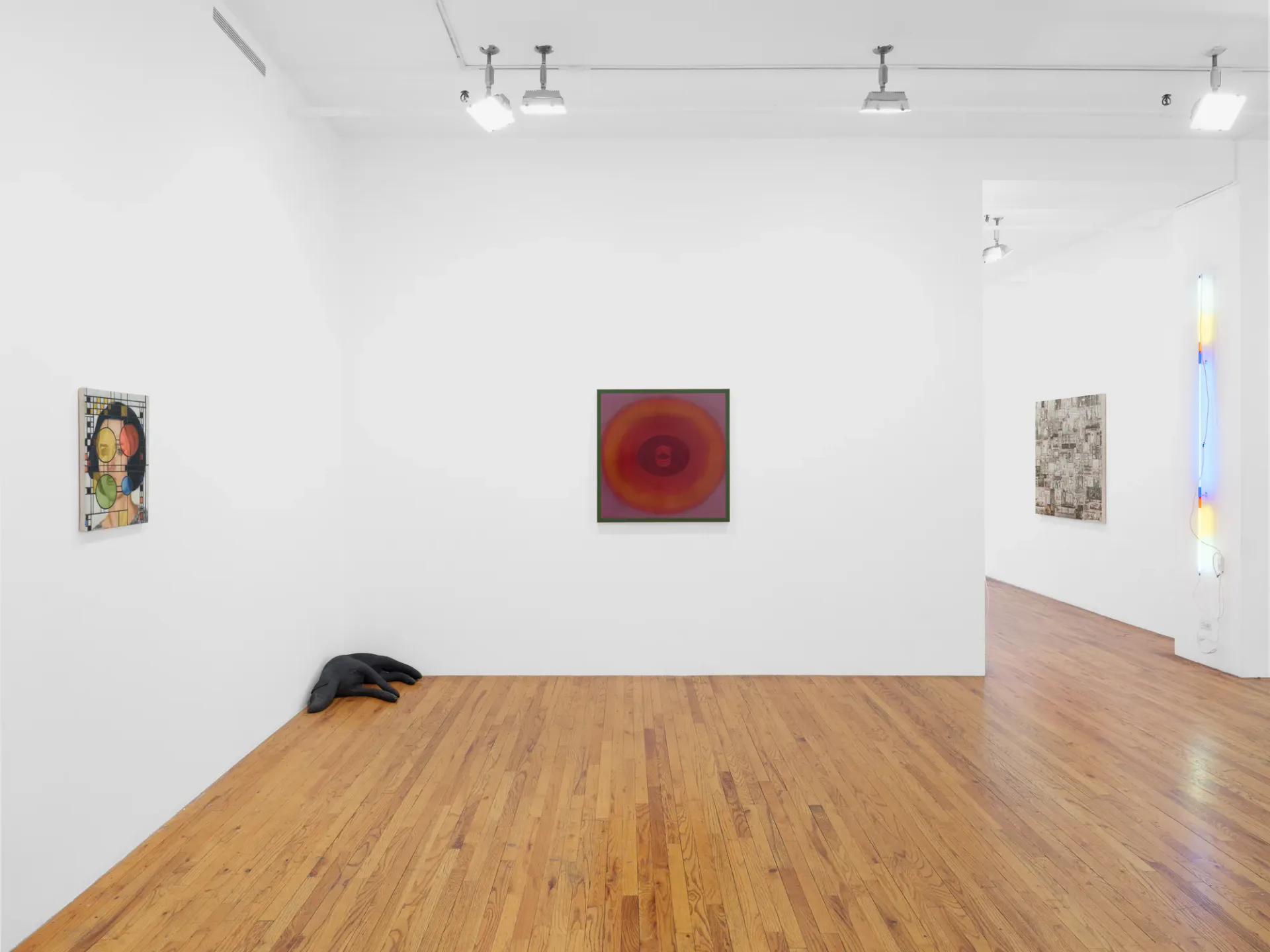 Gallery space with wooden floor, white walls, track lighting, four framed artworks including portrait and red abstract, neon light installation on right, dark sculpture on floor.
