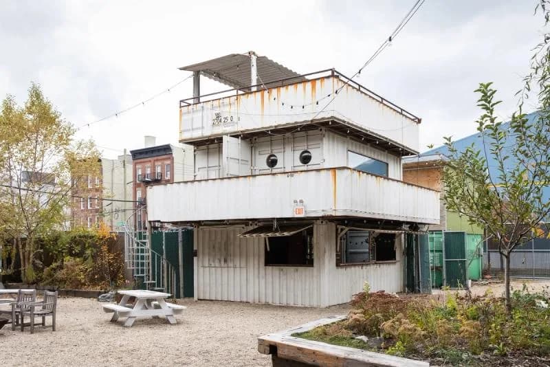 Exterior of stacked white and industrial metal structure building with multiple levels, rooftop platform, and surrounding landscape with benches.
