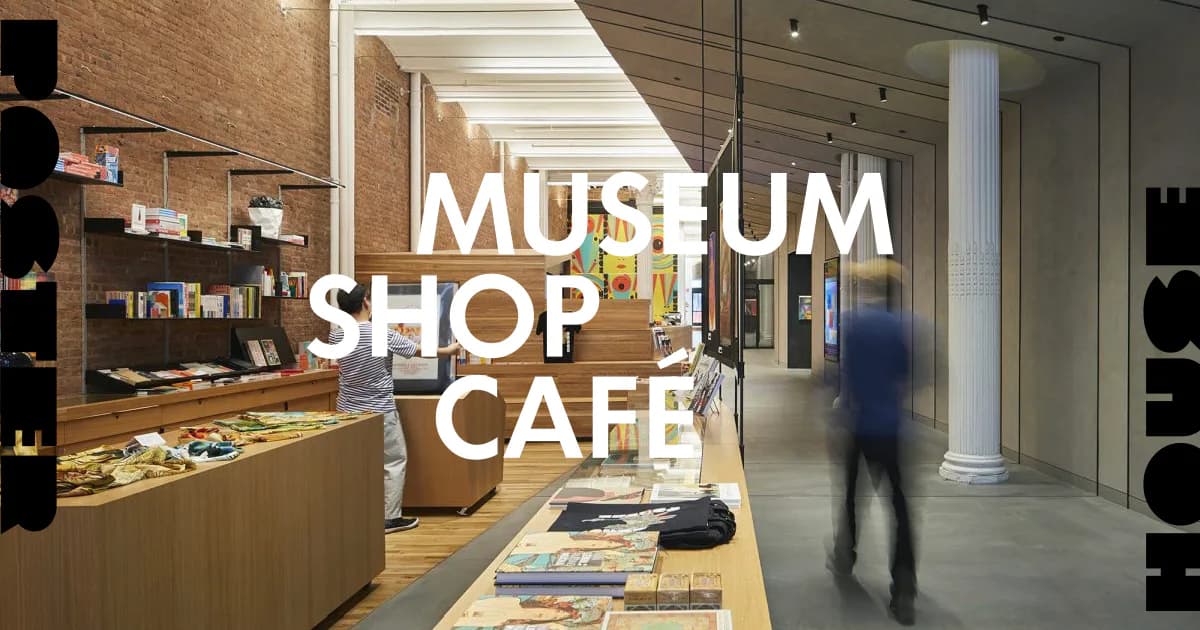 Interior of a modern museum shop and café with wooden display cases, shelving, polished floors, and a blurred figure walking through the space.