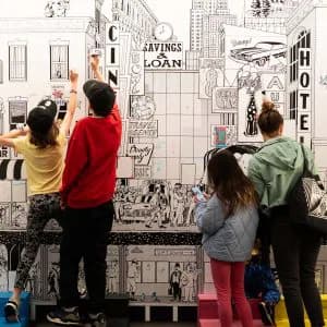 Gallery visitors of varying ages interacting with a large black-and-white illustrated mural or interactive artwork on a wall at Poster House.