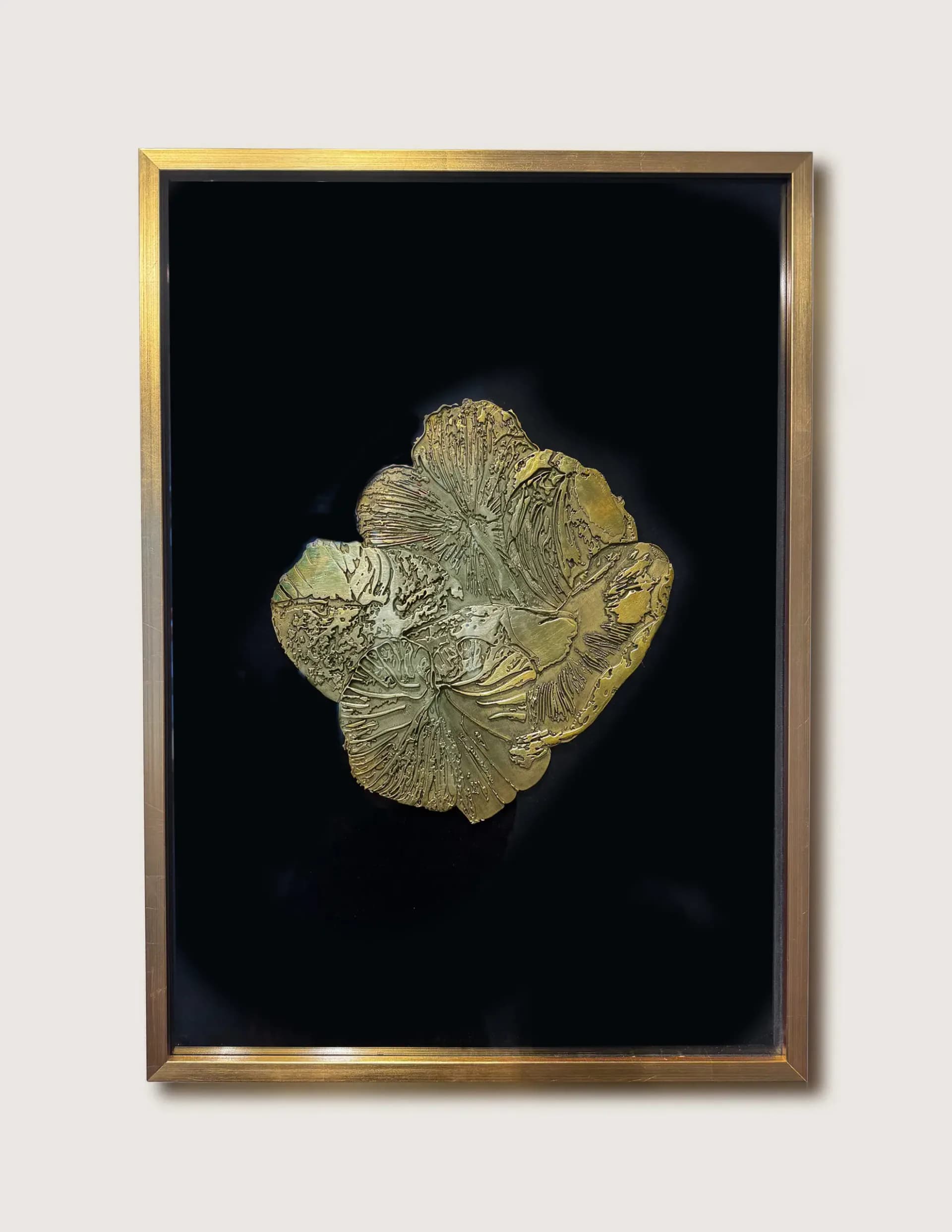 Gold-leaf sculptural form mounted on black background in gold-toned frame, with organic textured surface resembling flora or mineral structures.