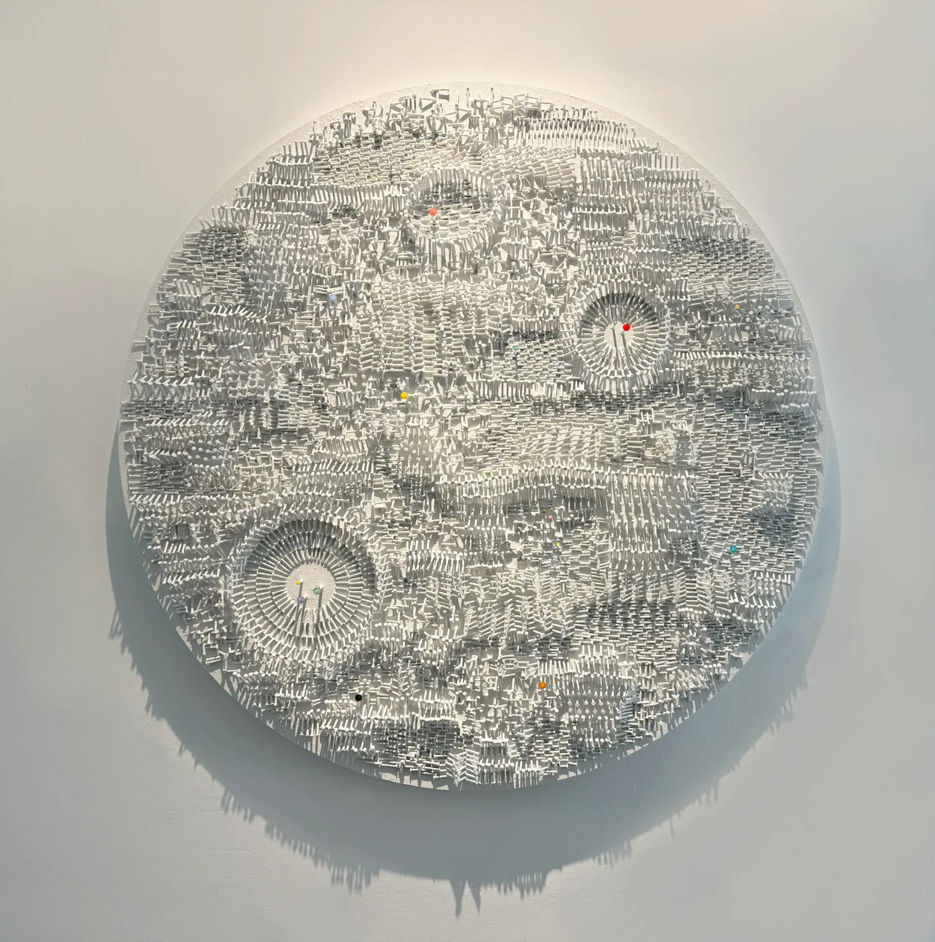 Circular paper-cut or carved relief artwork in monochromatic cream and grey, featuring intricate layered patterns with organic and geometric elements.