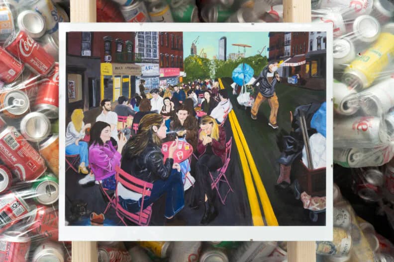 Mixed-media artwork combining photograph of crowded urban street scene framed in center with collaged images of discarded cans and refuse surrounding the border.