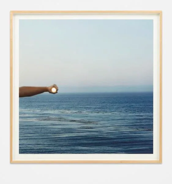 Framed photograph of a rusty metal pipe extending into calm blue ocean horizon under pale sky.