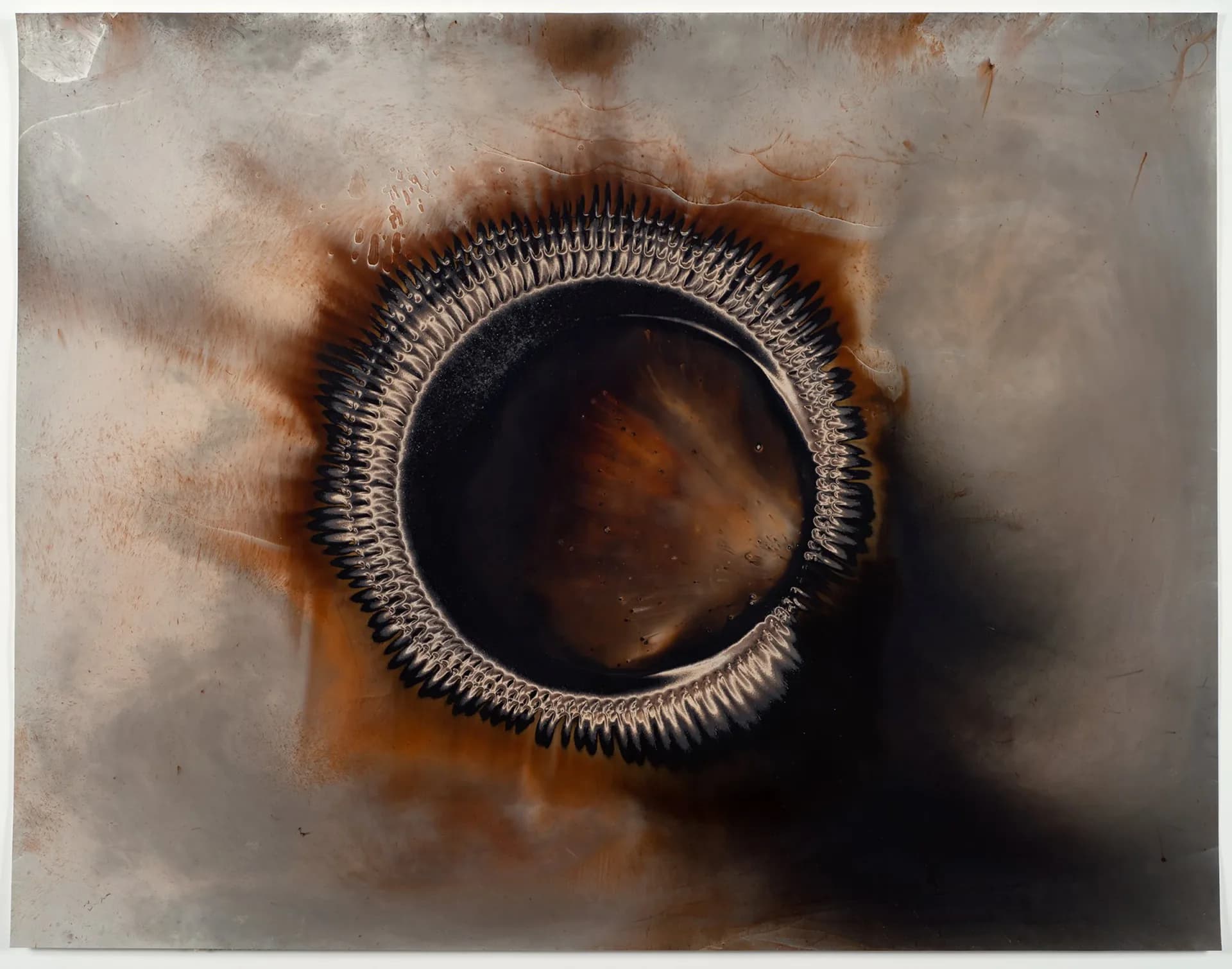 Mixed-media artwork featuring a dark circular form with textured concentric rings, surrounded by brown and gray atmospheric effects.