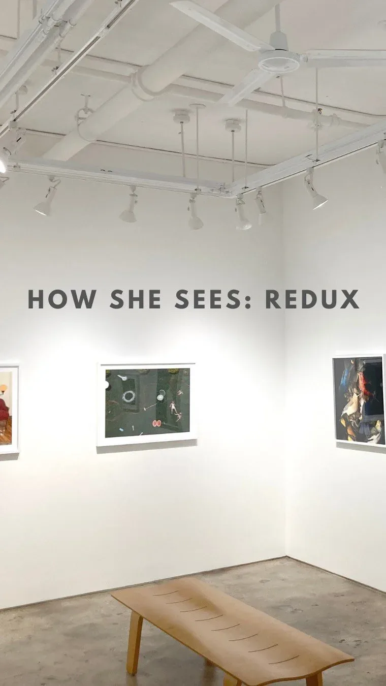 White gallery interior with track lighting and three artworks on walls; wooden bench in foreground; exhibition title 'How She Sees: Redux' visible.