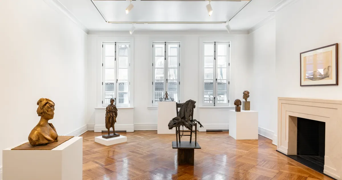 Bright gallery interior at Rosenberg & Co. with wooden floors, three tall windows, bronze sculptures on pedestals, a fireplace, and neutral white walls.