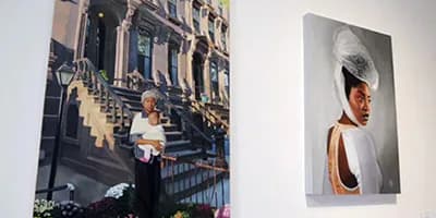 Interior gallery view showing two framed photographs on white walls—one large image of a woman on architectural steps, one portrait of a person wearing a white hat.