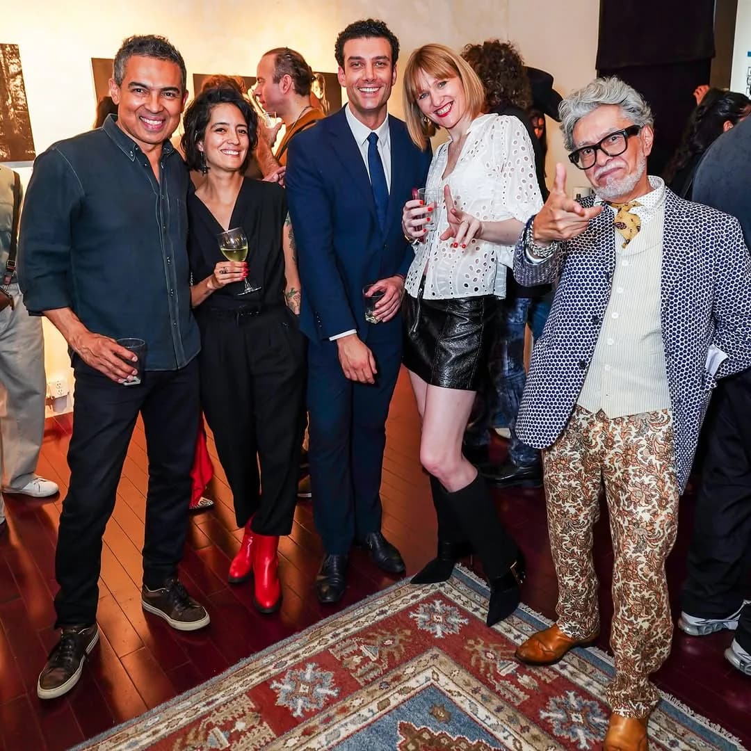 Five people gathered indoors at what appears to be a gallery or event space, with warm lighting and artwork visible in the background.