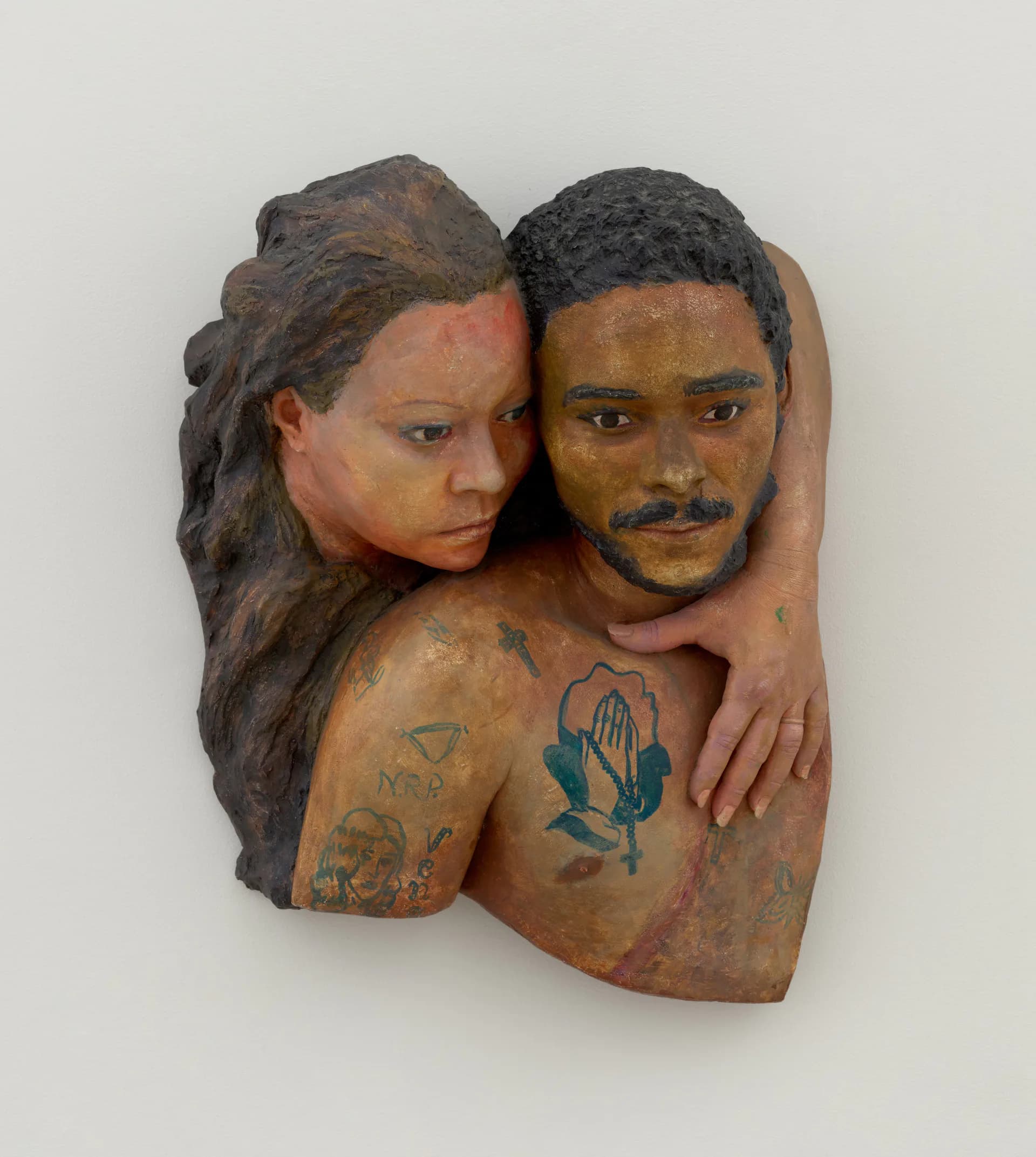 Sculptural bust depicting two figures embracing, with detailed facial features and tattooed shoulders, crafted in clay or ceramic with hand-painted details.