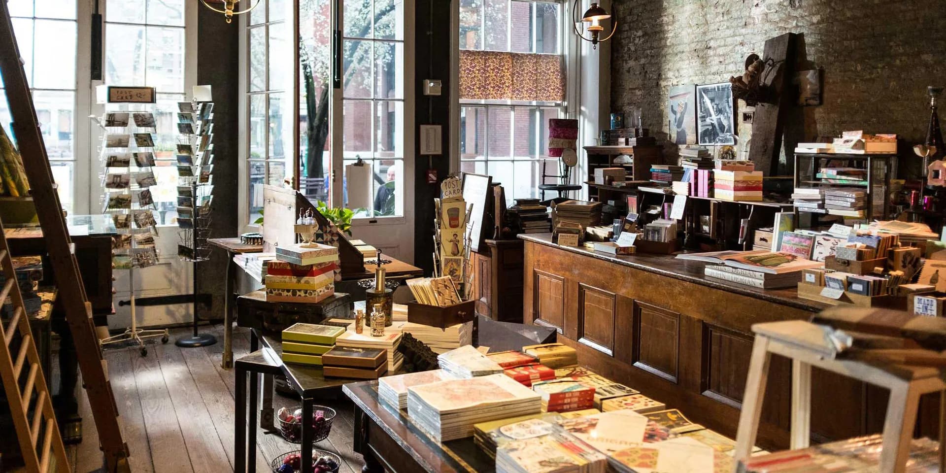 Interior of Seaport Museum New York shop with wooden furniture, shelving, counter display, and large windows showing street outside.