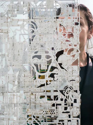 Large-scale translucent white paper-cut or laser-cut installation with intricate organic patterns, a person visible behind the artwork.