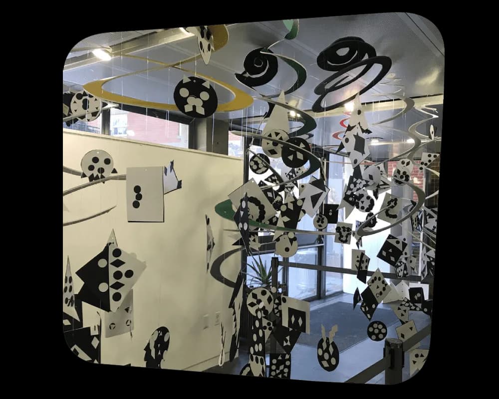 Large-scale mixed-media installation featuring black mechanical gears and film reels suspended and mounted on cream-colored walls, exploring themes of motion and cinema.