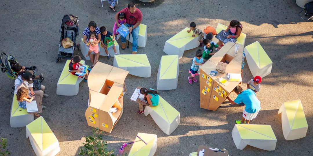 Overhead view of colorful modular yellow and orange seating/platform structures arranged in a public plaza with children and adults engaging in play and activities.