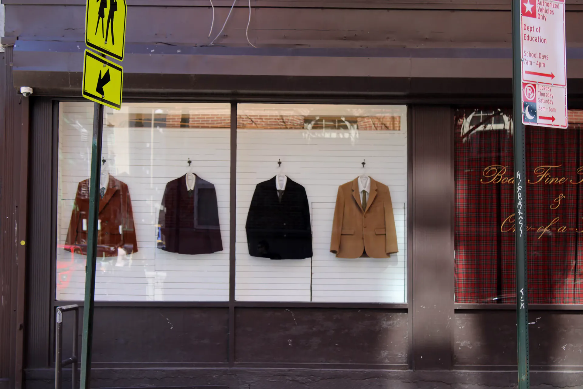 Storefront window display with four vintage jackets and blazers in brown, black, and tan on dress forms against white background.