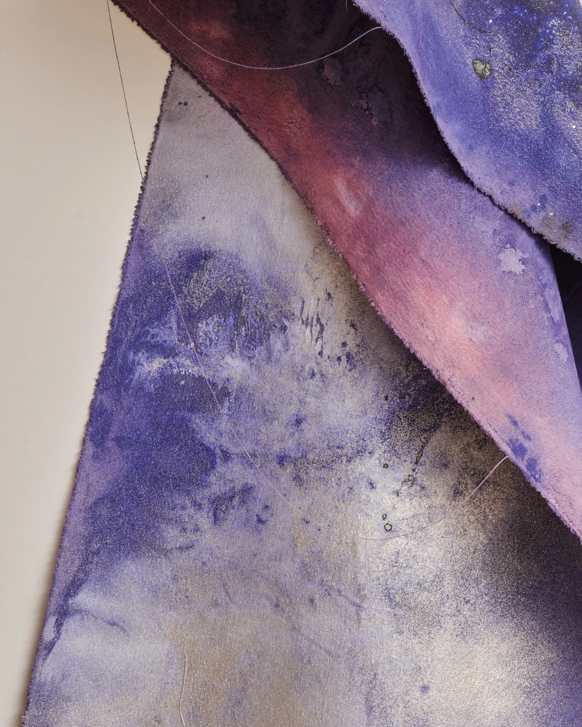 Abstract mixed-media work featuring layered fabric or paper in purple, pink, maroon, and gray tones with translucent overlapping planes.
