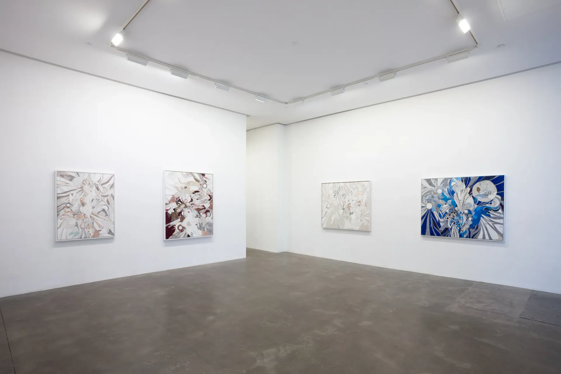 Gallery corner view showing four framed botanical artworks on white walls with track lighting and polished concrete floor.
