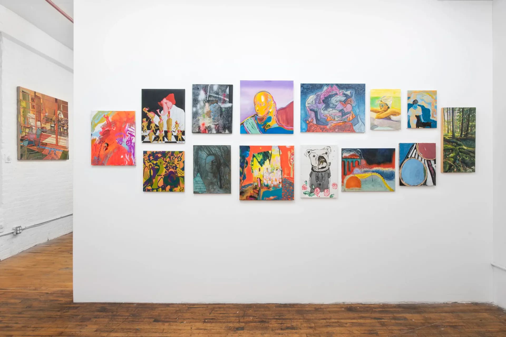 Gallery wall at Tappeto Volante Gallery displaying approximately eighteen small to medium colorful paintings arranged in organic cluster against white wall.