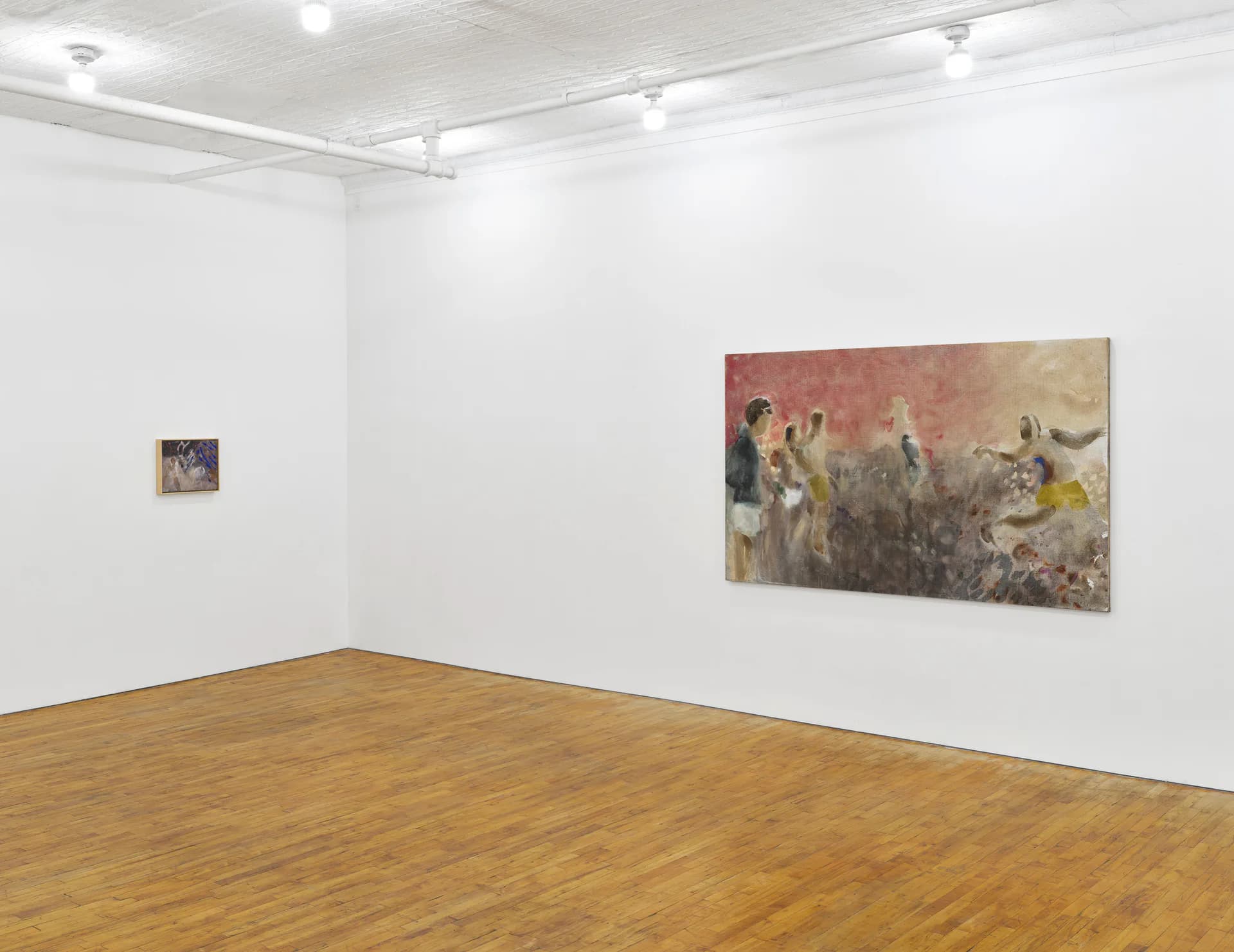 Minimalist gallery interior with white walls and wooden floor displaying two framed mixed-media works: a small piece on left wall and larger work on right wall.