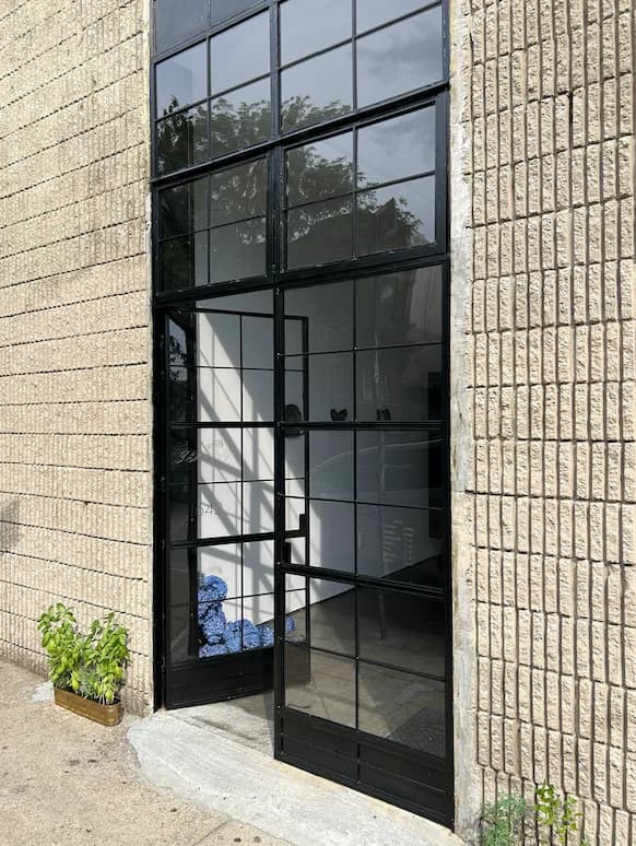 Photograph of Tempest Gallery storefront: black metal-framed glass doors and windows in brick building exterior, Ridgewood.