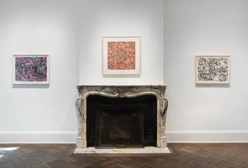 Interior photograph of The Elkon Gallery showing three small framed abstract artworks on white walls flanking a marble fireplace mantel.