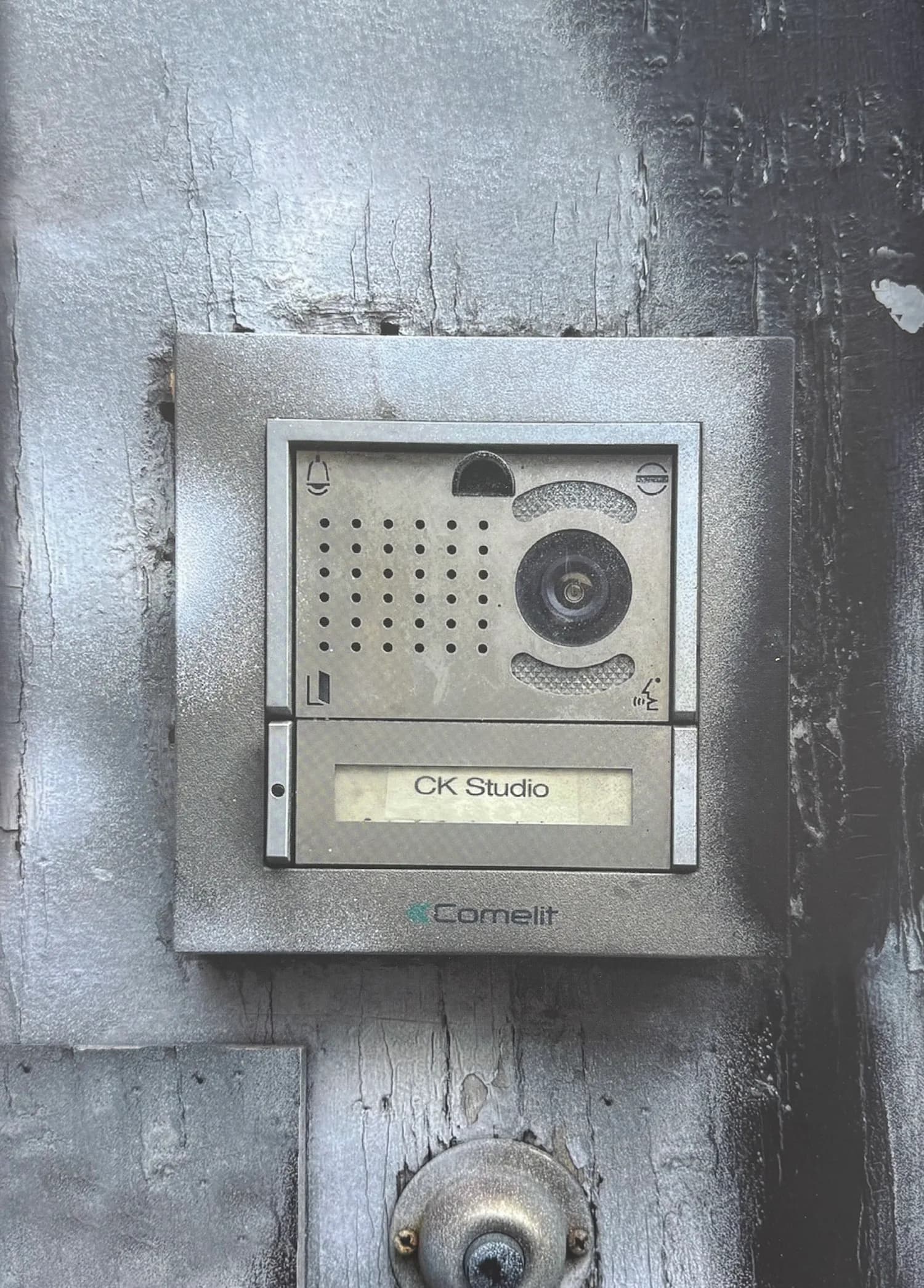 Weathered metal intercom unit labeled 'CK Studio' and 'Cornelit' mounted on a textured gray exterior wall.