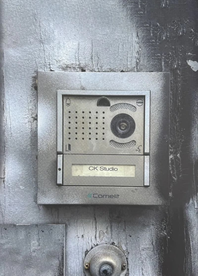 Weathered metal intercom unit labeled 'CK Studio' and 'Cornelit' mounted on a textured gray exterior wall.
