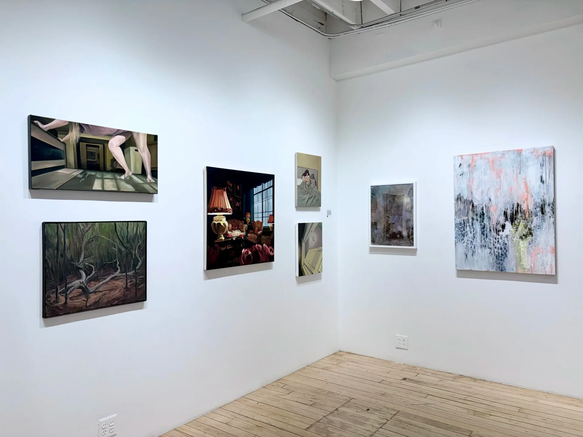 The Painting Center gallery corner with light wood floors, white walls, and mixed-media artworks including photographs, paintings, and mixed-media pieces hung asymmetrically.