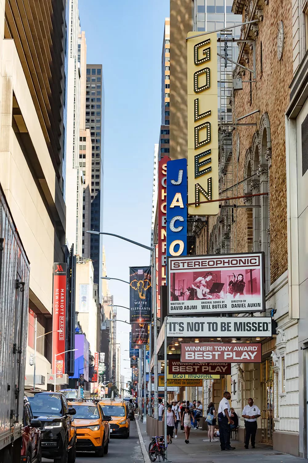Pedestrian theater district street lined with marquees and historic building facades, including JACO and GOLDEN theater signs, yellow cabs visible.