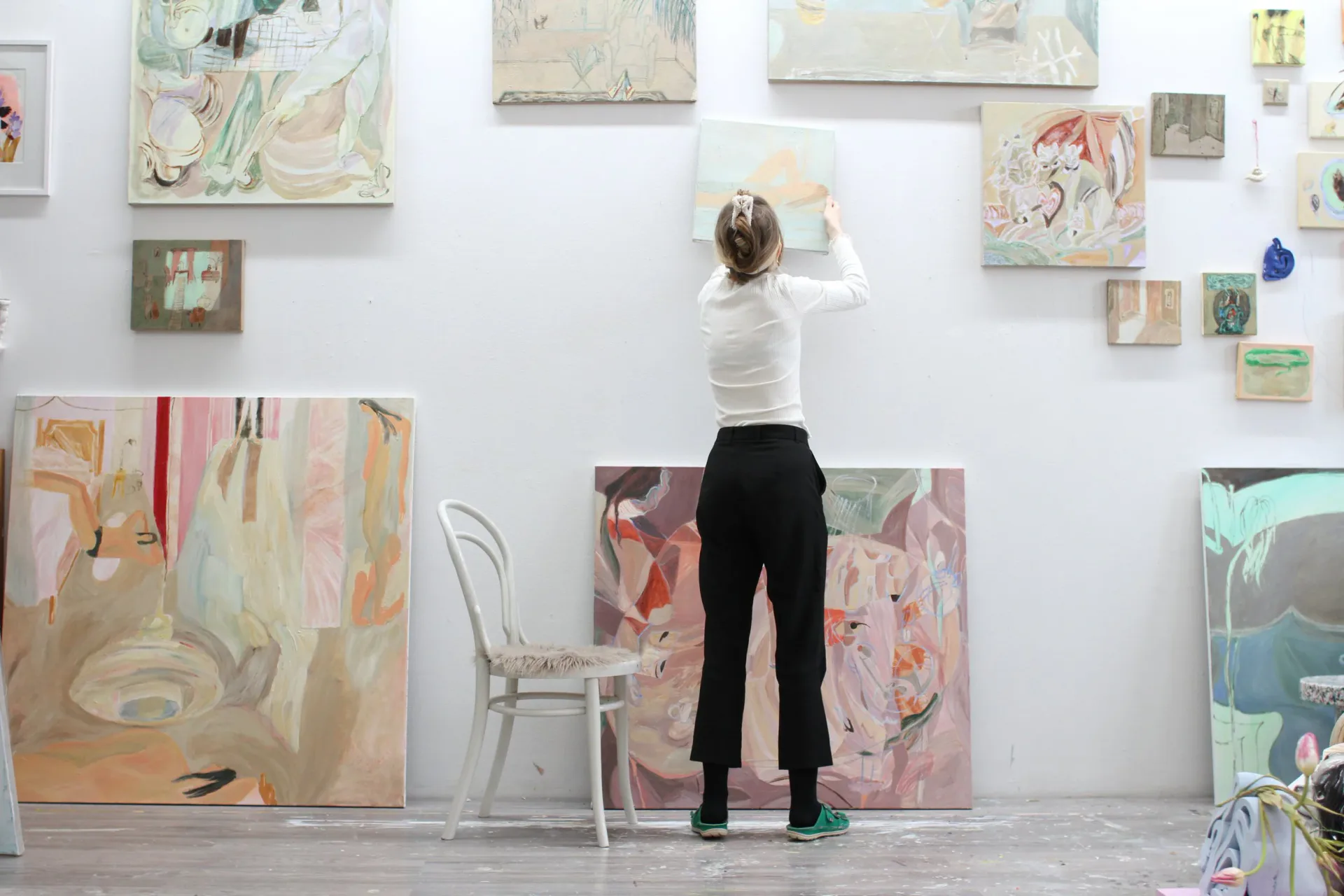 Interior view of Triangle Arts Association gallery with a person standing viewing multiple artworks displayed on white walls, including paintings and smaller works at varying heights.