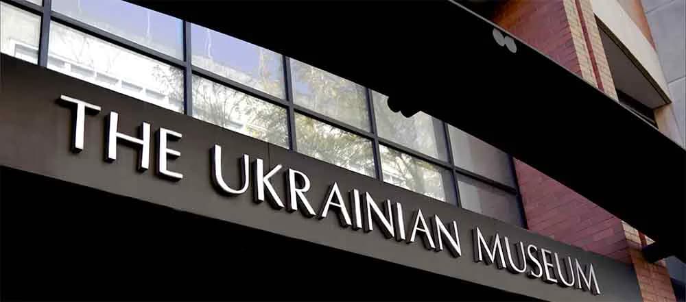 Storefront signage reading 'THE UKRAINIAN MUSEUM' in white letters on dark background with illuminated window displays above.