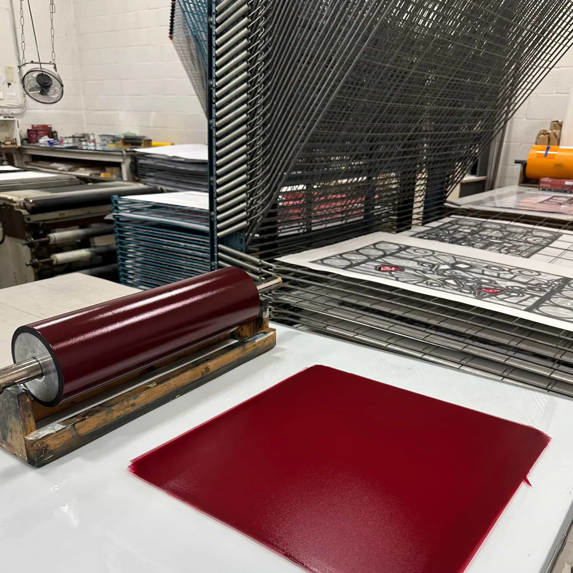 Deep burgundy rectangular print or material sample on white surface with printing equipment and stacked papers visible in printmaking studio background.