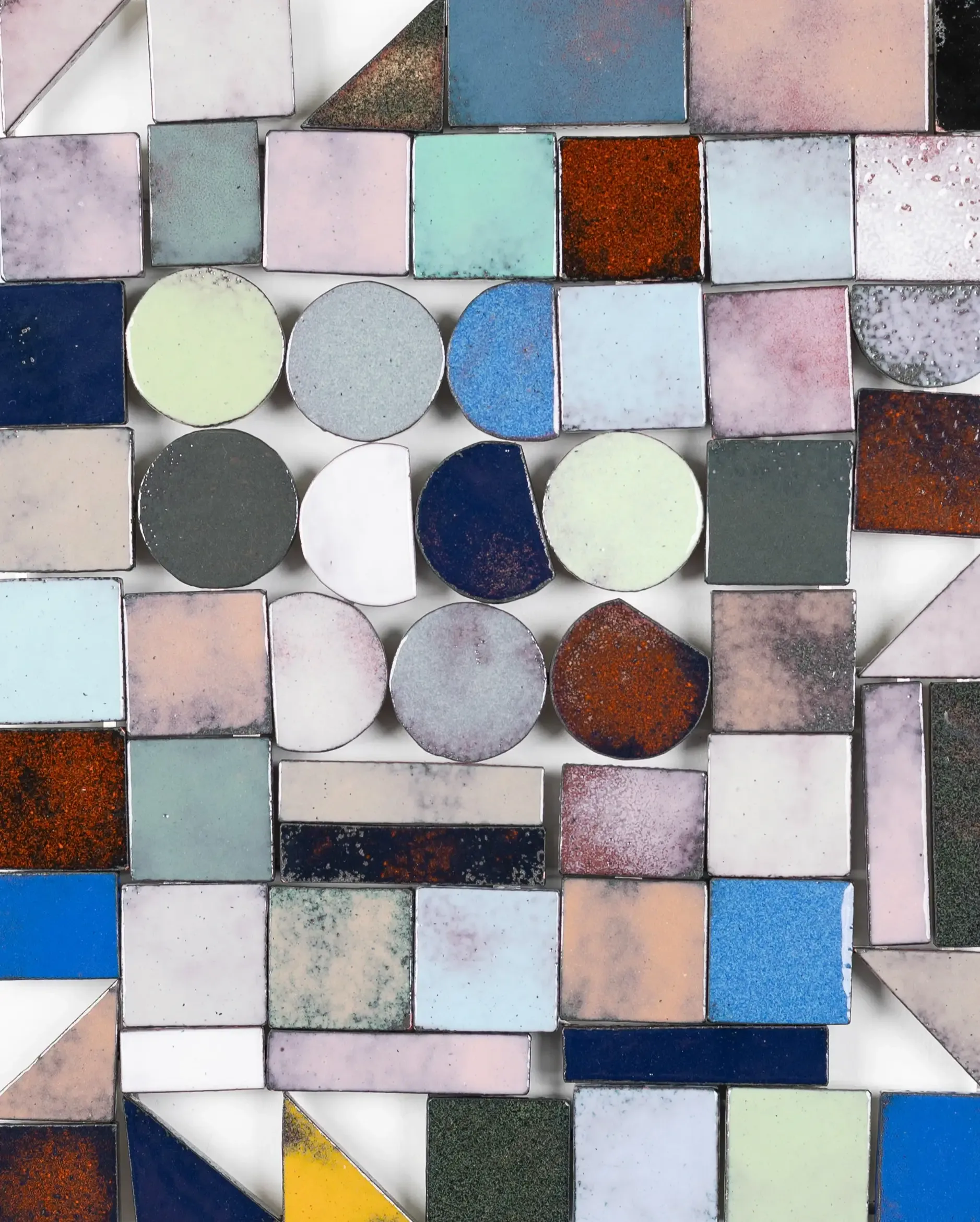 Layered mixed-media composition featuring ceramic tiles, circular elements, and rectangular tiles in dusty pink, blue, rust, and neutral tones with varied surface textures.