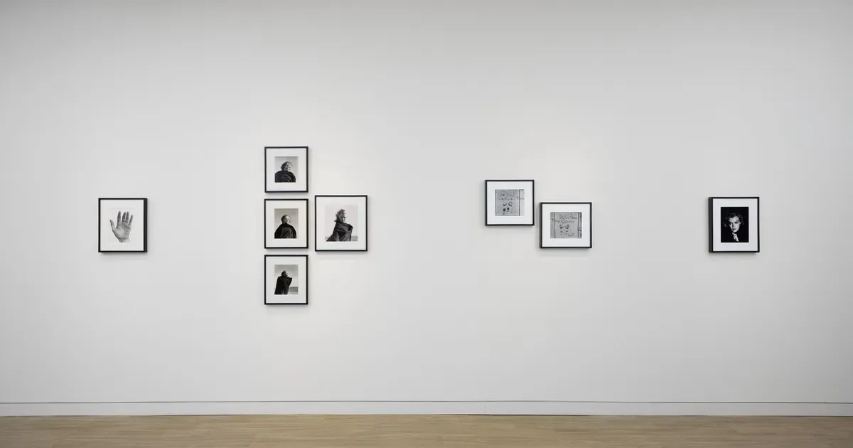 Gallery wall displaying a collection of small framed prints with hand and geometric motifs arranged in groups across white wall space.