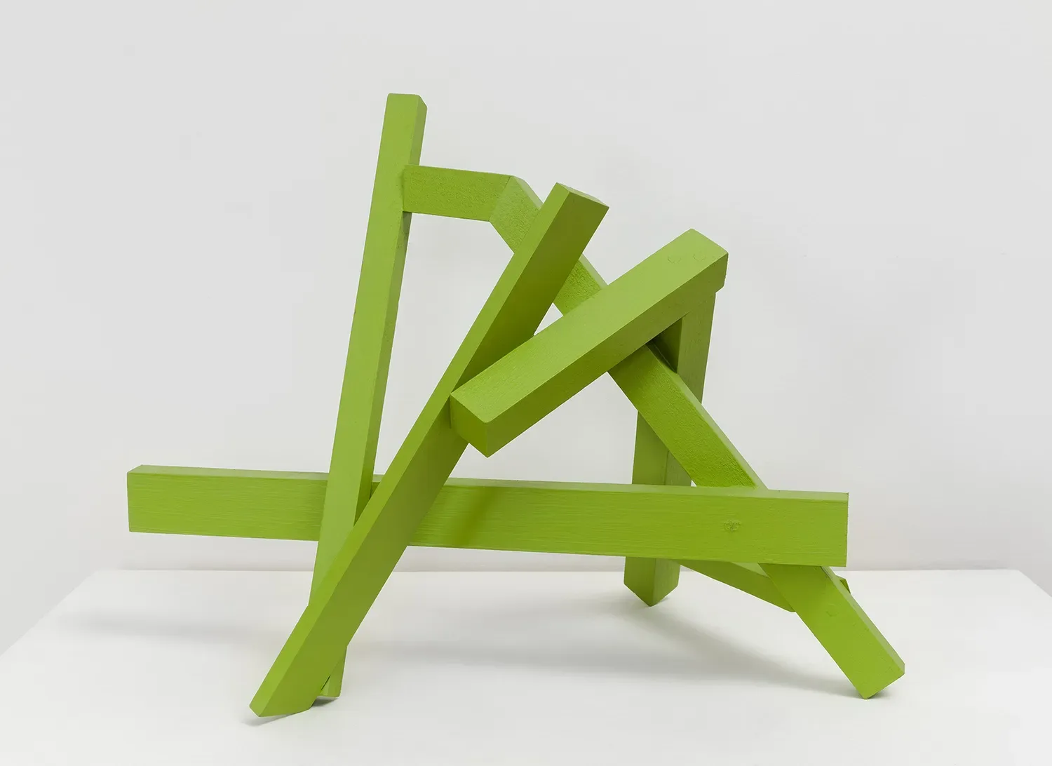 Abstract lime-green wooden sculpture with intersecting angular planes and geometric forms on white surface.