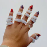 Hand wearing five white glass rings with embedded red and earth-tone decorative elements.